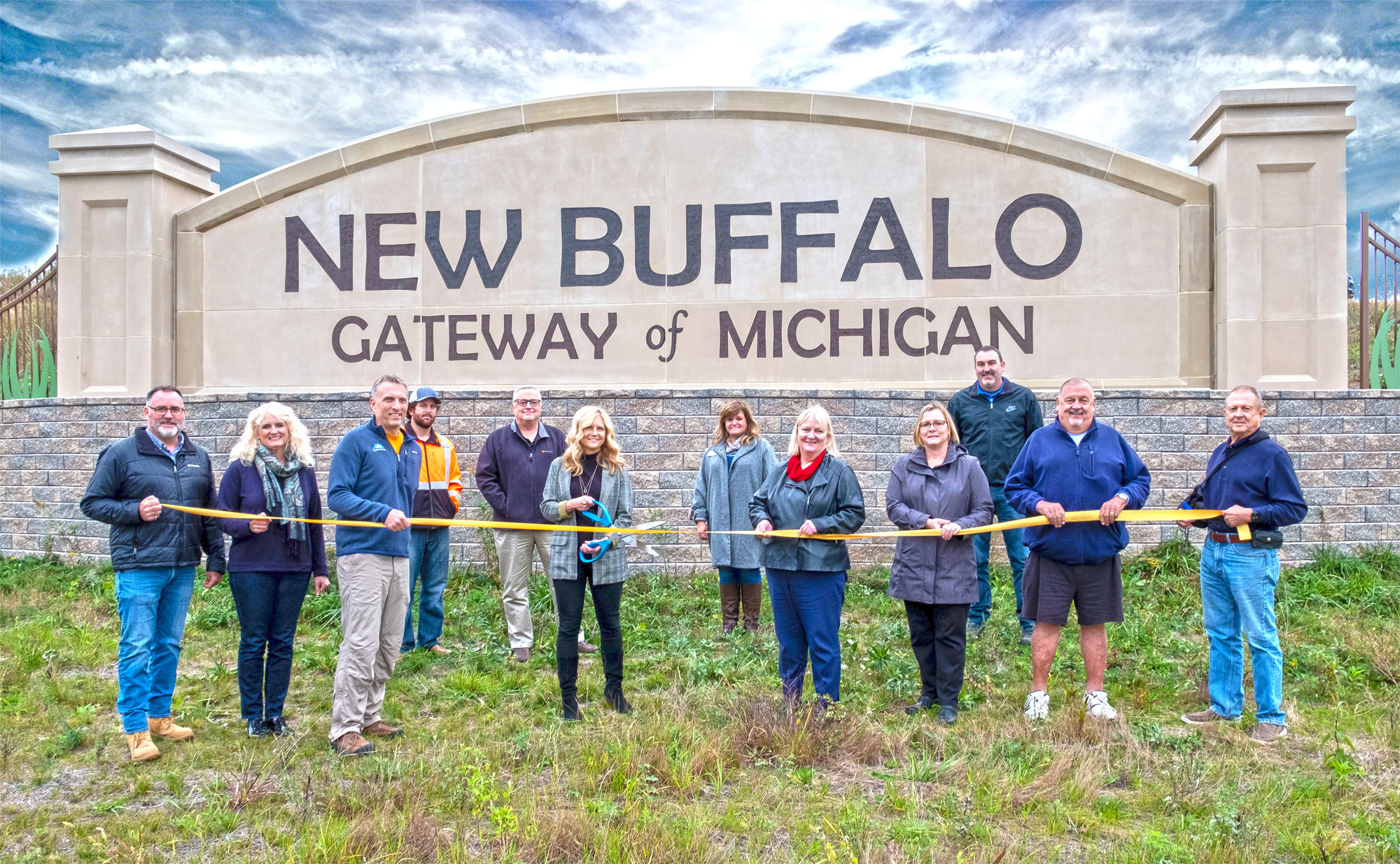 Group of individuals standing in front of the New Buffalo - Gateway of Michigan logo